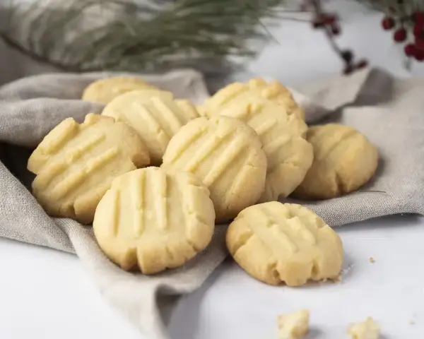 Montón de galletas de mantequilla doradas con líneas marcadas, servidas sobre una tela gris.