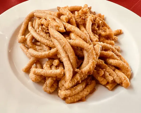 Pici all'aglione, uno dei piatti tipici di Arezzo, serviti su un piatto bianco.