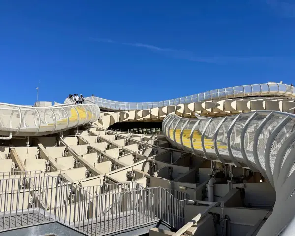 The Metropol Parasol, known as Las Setas de Sevilla, features a modern wooden structure with winding walkways and yellow steps under a clear blue sky.