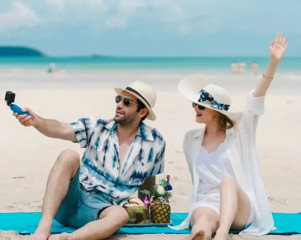 Para na plaży nagrywa filmik kamerką GoPro, a jego partnerka macha do obiektywu. Idealne wakacje pod gruszą!