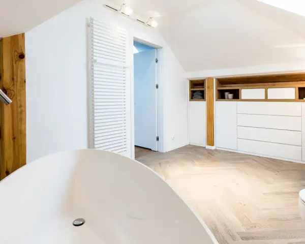 Élégante salle de bain sous pente avec baignoire îlot, lavabo, toilettes et rangements en bois.