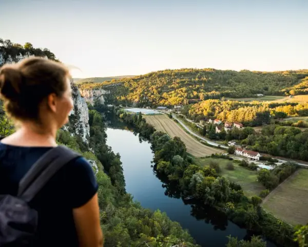 Une femme admire un paysage de carte postale lors de son voyage découverte en France. La rivière serpente à travers des collines verdoyantes et des villages pittoresques.