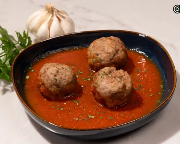 Tres albóndigas caseras en una rica salsa de tomate, adornadas con perejil fresco. Un plato reconfortante que evoca la cocina tradicional.