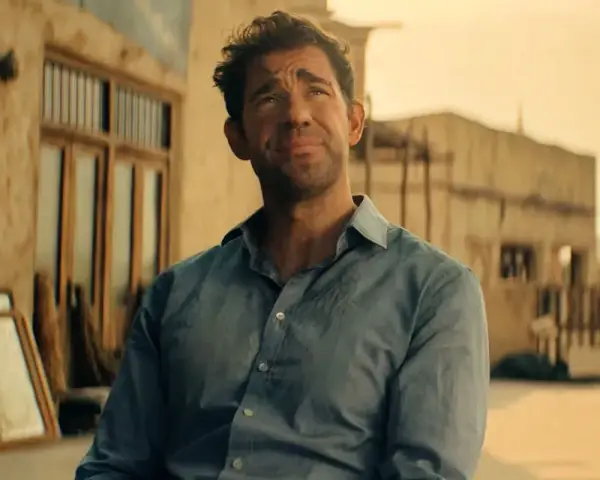 John Krasinski w niebieskiej koszuli, zamyślony. Widzimy fragmenty jego filmów, seriali i programów.