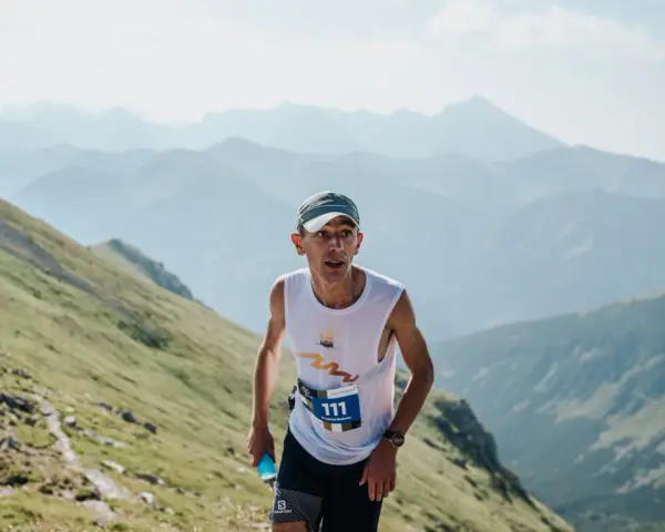 Zawodnik z numerem 111 biegnie pod górę podczas Tatra Sky Marathon. W tle piękne, mgliste pasmo górskie.