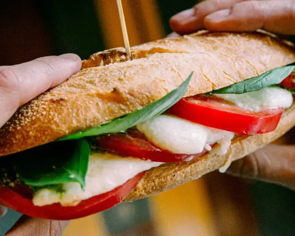 Ręce trzymają pyszne włoskie pieczywo z mozzarellą, pomidorami i bazylią. Idealne na szybki lunch.