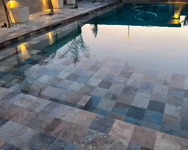 Escalones de piscina con diversos tipos de gresite para piscinas, creando un mosaico de tonos grises, azules y marrones.