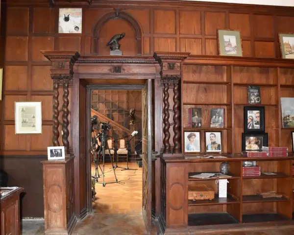 Wnętrze biblioteki w **zamku w Lubniewicach**. Drewniane boazerie, regały z książkami i portretami, a w przejściu widok na schody i sprzęt nagraniowy.