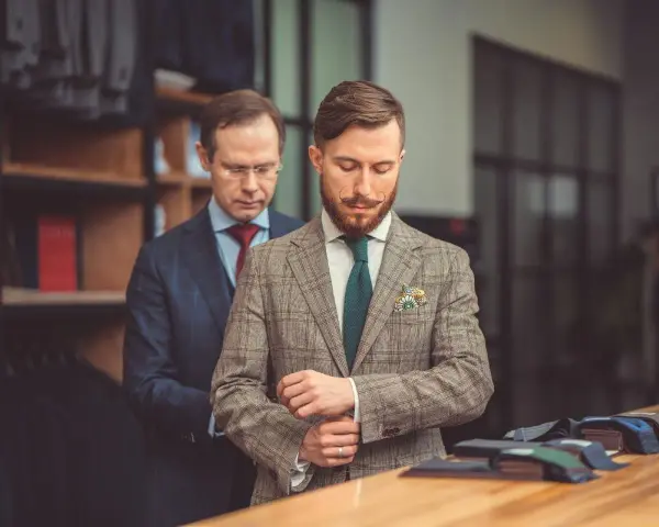 Elegancki garnitur dla świadka, dopasowywany przez krawca. Mężczyzna z wąsikiem przymierza tweedową marynarkę w kratę.