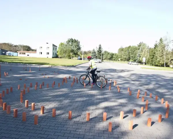 Młody rowerzysta w kamizelce odblaskowej i kasku pokonuje tor przeszkód z palików, przygotowując się do egzaminu na kartę rowerową.