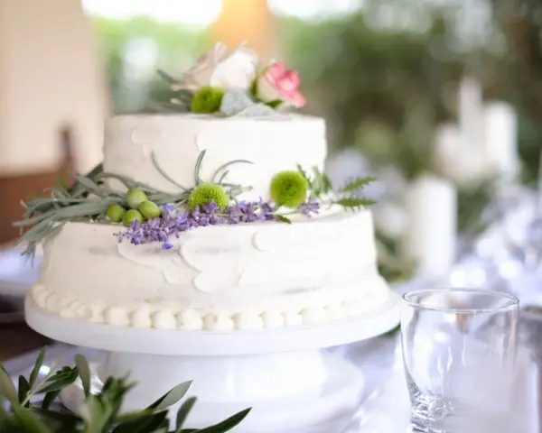 Dwupoziomowy tort weselny ozdobiony kwiatami, ziołami i oliwkami. Delikatne kremowe wykończenie i naturalne dekoracje podkreślają wyjątkowe smaki tortów weselnych.