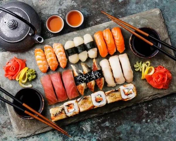 Piękny zestaw sushi: nigiri z łososiem, krewetkami, tuńczykiem i węgorzem, a także rolki. Obok czajniczek i filiżanki z herbatą. Idealne na co do sushi.