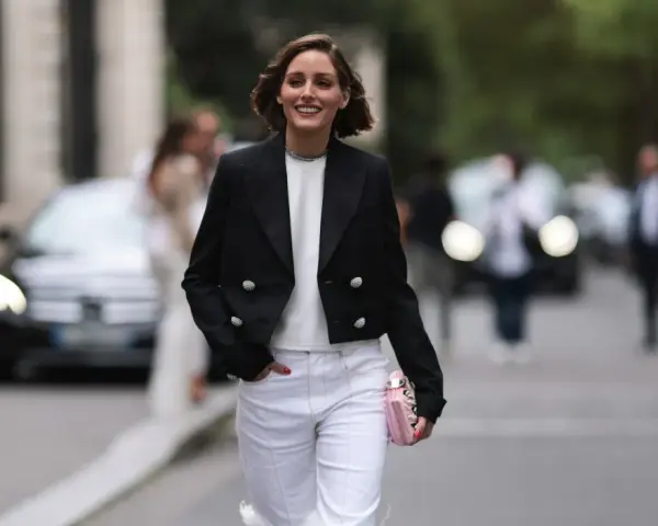 Mujer sonriente con chaqueta negra y pantalones blancos, lista para una comida familiar de invierno.