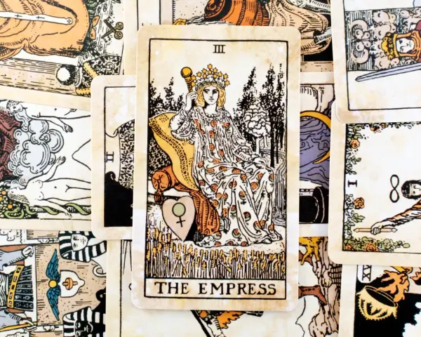 Karta cesarzowa tarot, przedstawiająca kobietę w koronie na tronie, otoczona innymi kartami.
