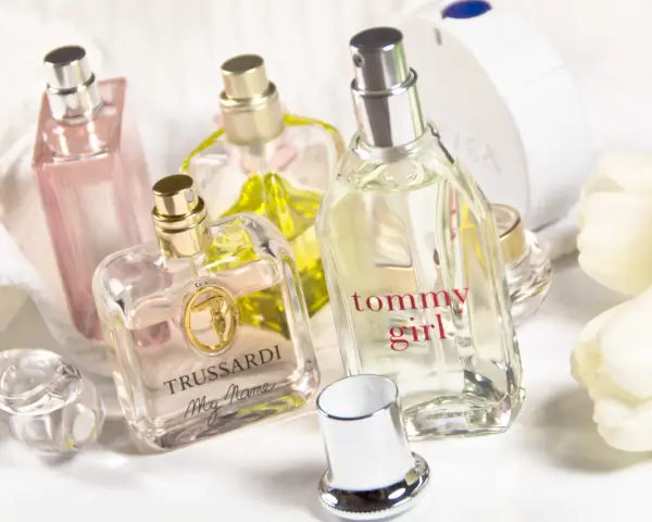 Mehrere Parfümflaschen, darunter Trussardi und Tommy Girl, auf weißem Handtuch mit weißen Tulpen.