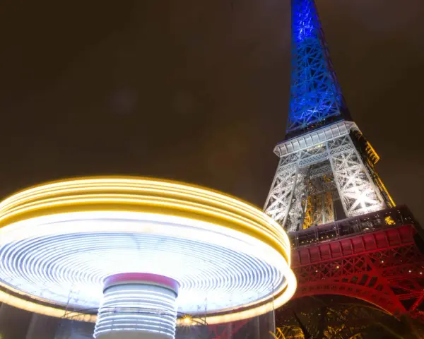 Manège lumineux tournant devant la Tour Eiffel illuminée en bleu, blanc et rouge. Une scène de Paris nocturne, parmi les plus belles photos de nuit.