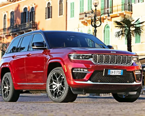 Czerwony Jeep Grand Cherokee zaparkowany na brukowanej ulicy przed budynkami z balkonami.