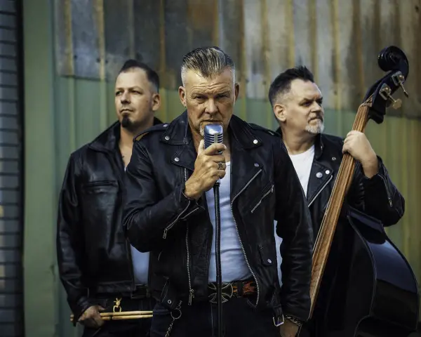 Rock n roll band in Lederjacken. Sänger hält Mikrofon, Bassist spielt Kontrabass, Schlagzeuger hält Sticks.