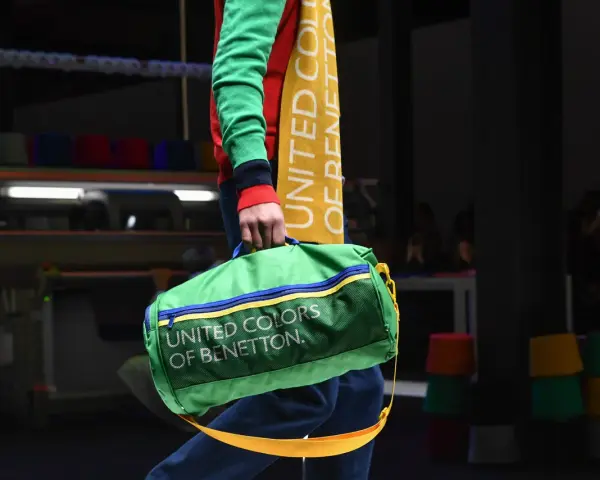 Zielony worek z napisem "UNITED COLORS OF BENETTON" niesiony przez modela w kolorowym swetrze.