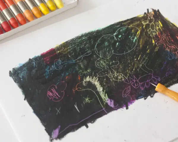 Un niño empieza a dibujar con ceras sobre un papel negro, revelando colores vibrantes y figuras fantásticas.
