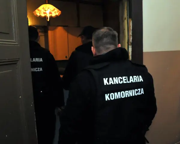 Komornicy w kamizelkach z napisem "KANCELARIA KOMORNICZA" wchodzą do pomieszczenia. Pytanie o alimenty na dziecko ile procent z wynagrodzenia może być związane z ich pracą.