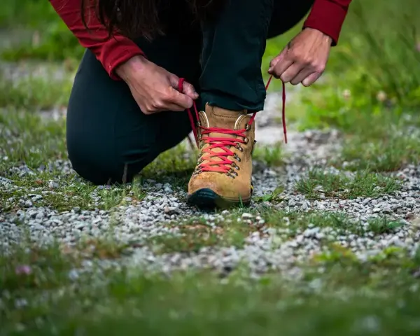 Osoba klęczy i sznuruje brązowy but trekkingowy z czerwonymi sznurówkami. To dobry przykład, jak zmierzyć stopę przed zakupem obuwia.