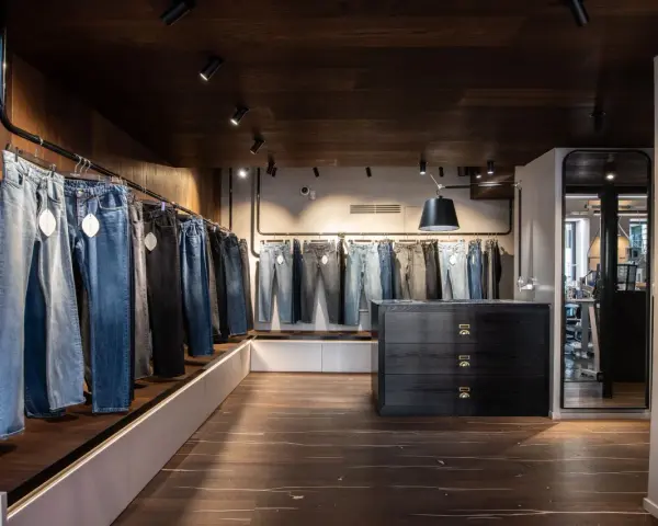 Jeans in vari lavaggi e tagli, inclusi modelli slim fit, esposti in un negozio moderno con pavimenti in legno scuro e illuminazione a faretti.