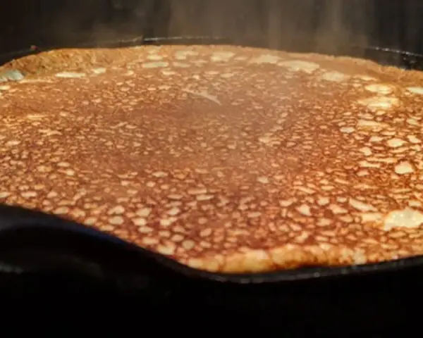 En gyllene, nygräddad pannkaka steker i en gjutjärnspanna. Perfekt för en glutenfri frukost eller fika.