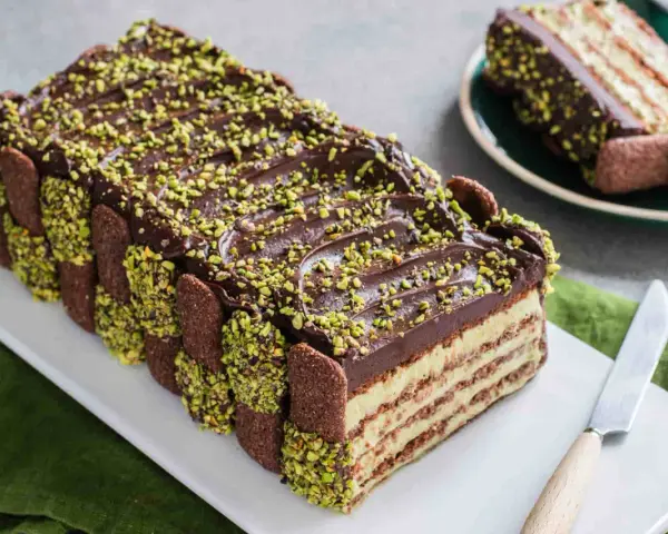 Torta fredda con strati di biscotti, crema e cioccolato, decorata con granella di pistacchio. Un tripudio di dolci al pistacchio.