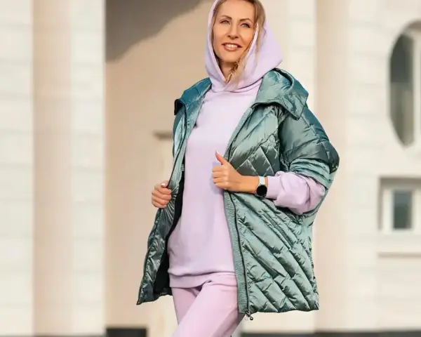 Uśmiechnięta kobieta w pastelowym komplecie dresy z wysokim stanem damskie i błyszczącej kurtce.