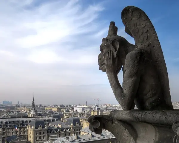 Stryge de Notre Dame, pensif, contemple Paris sous un ciel bleu et nuageux.