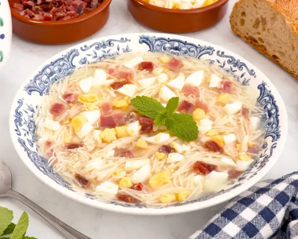 Sopa de picadillo andaluza en un plato azul y blanco con trocitos de huevo duro, jamón y fideos finos.