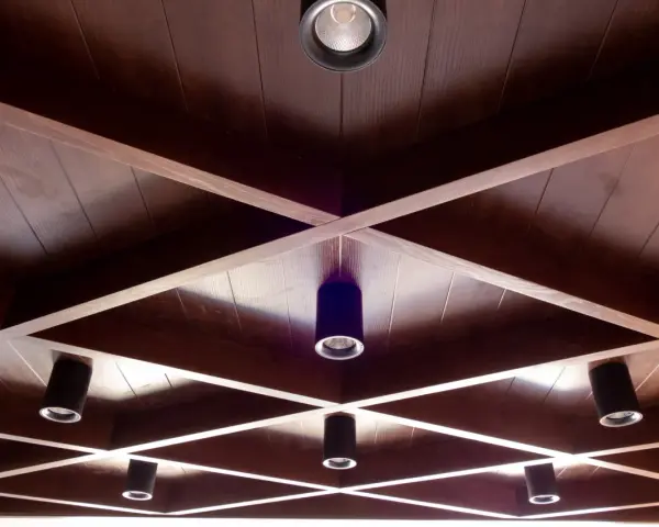 Drewniane, kratownicowe **stare kasetony na suficie** z wbudowanymi reflektorami tworzą geometryczny wzór.
