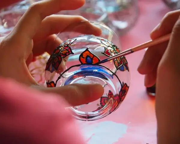 Manos pintando un vaso de cristal con flores de colores. Aprende como pintar cristal a mano y crea arte.