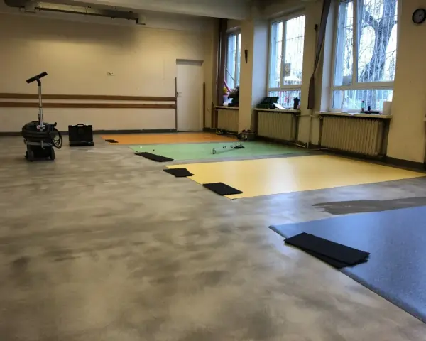 Przygotowanie podłogi pod wykładzinę PCV: odkurzacz przemysłowy i kolorowe maty czekają na ułożenie.