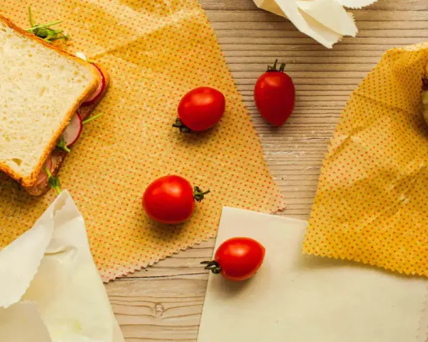 Un sandwich, des tomates et un morceau de fromage sont présentés sur des bee wraps maison à pois rouges sur fond de bois.