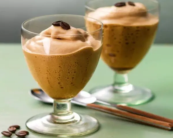Due bicchieri di spumone al caffè, guarniti con chicchi di caffè, su un tavolo verde.
