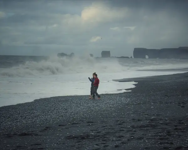 Para spaceruje po czarnej plaży Islandii, podczas gdy fale rozbijają się o brzeg.