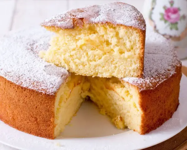 Una soffice torta fredda allo yogurt, spolverata di zucchero a velo, con una fetta sollevata che ne rivela la morbidezza.
