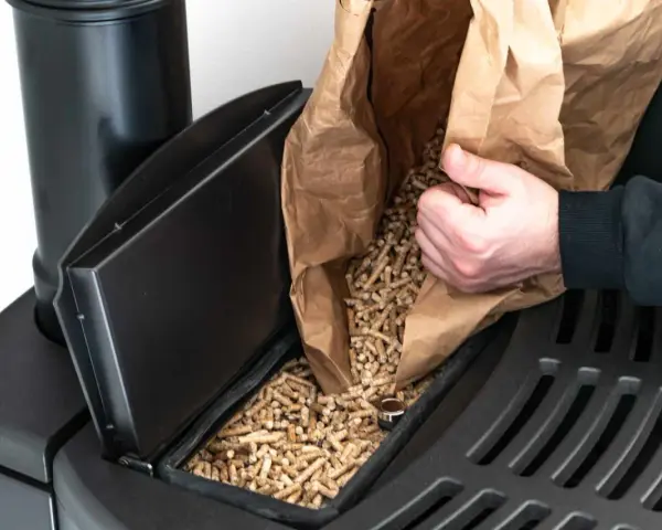 Persona rellena un compartimento de estufa de pellets. Considera el instalar estufa pellets precio para un hogar eficiente.
