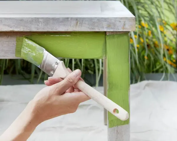 Mano pintando un escritorio de madera con pintura verde brillante, dándole un toque fresco y moderno.