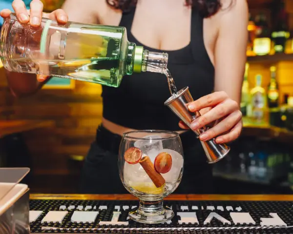 Barman nalewa alkohol z butelki do miarki nad kieliszkiem z lodem i owocami.