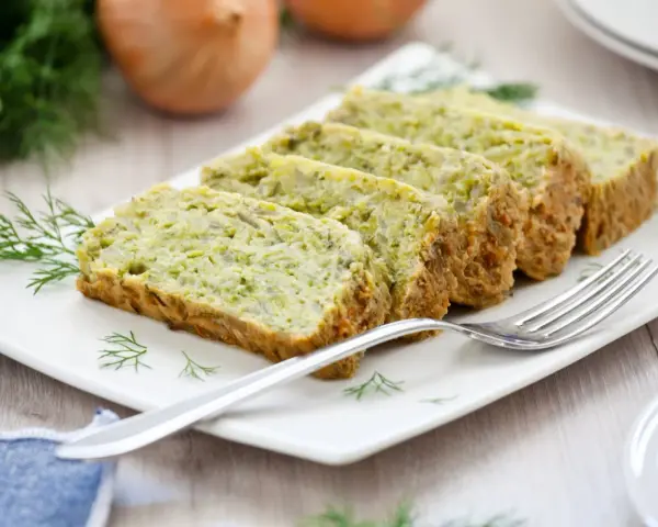 Fette di flan di zucchine su un piatto bianco, guarnite con aneto. Una forchetta argentata è appoggiata sul piatto.