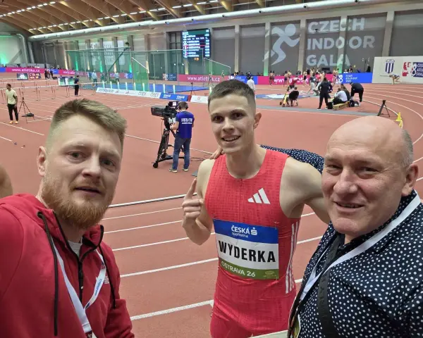 Trzej mężczyźni na bieżni lekkoatletycznej. W środku zawodnik Maciej Wyderka w stroju sportowym.