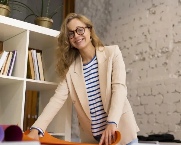 Uśmiechnięta kobieta w beżowej marynarce i pasiastym T-shircie, z okularami na nosie. Jej strój to przykład profesjonalnego dress code nauczyciela.
