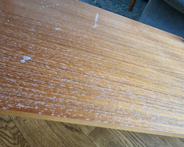 Detaljerad bild av en sliten teakskiva, redo för att renovera teakbord. Vita fläckar och repor syns tydligt.