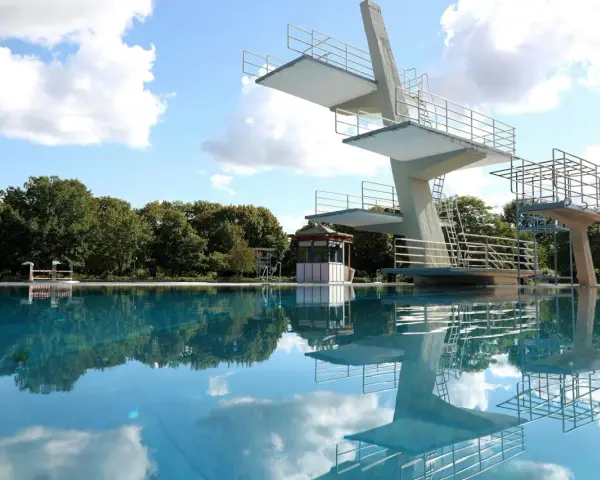 Sprungturm im Schwimmbad Pankow spiegelt sich im klaren Wasser. Ein sonniger Tag lädt zum Sprung ein.