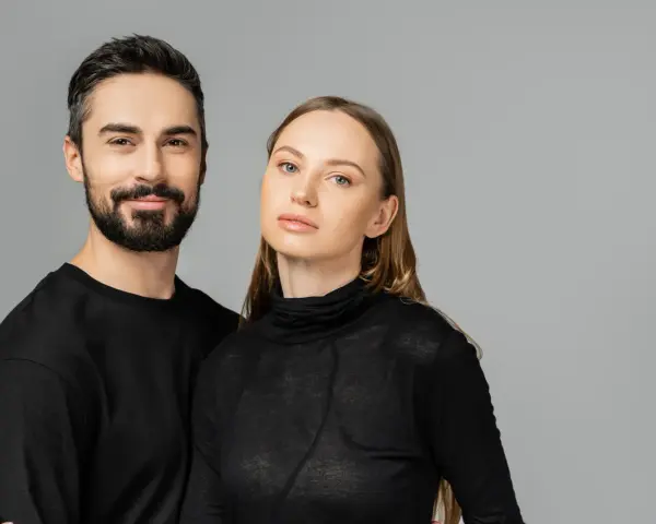 Para, która wygląda jakby mogła nosić ubrania unisex. Mężczyzna z brodą i kobieta z długimi włosami, oboje w czarnych, prostych ubraniach.