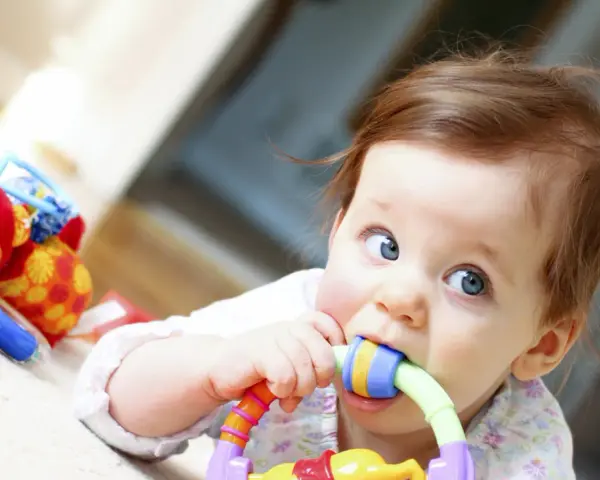 Bébé curieux mordillant un jouet coloré, dans le cadre d'un projet d'accueil individualisé pour son développement.