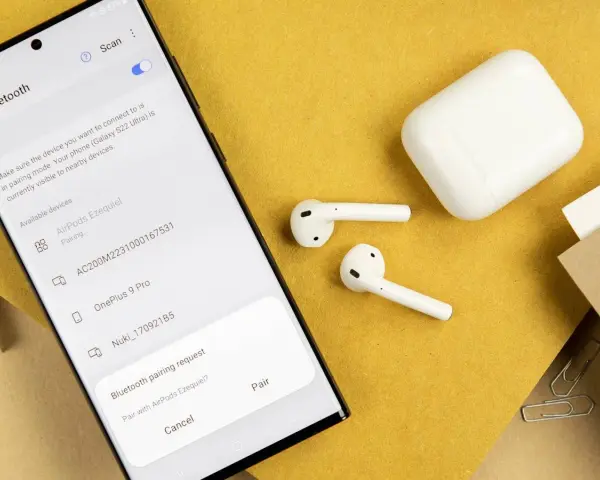 Samsung-Smartphone zeigt Bluetooth-Kopplungsanfrage für AirPods an, daneben liegen AirPods und Ladecase.